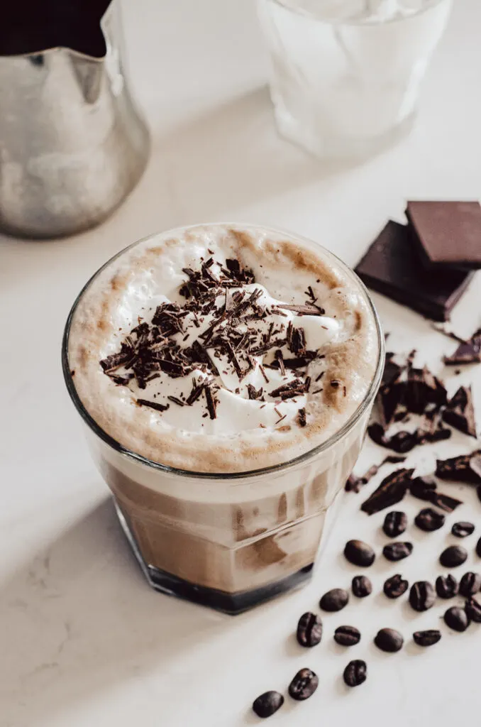 A glass filled with a mocha latte with coffee beans and chocolate off to the side.