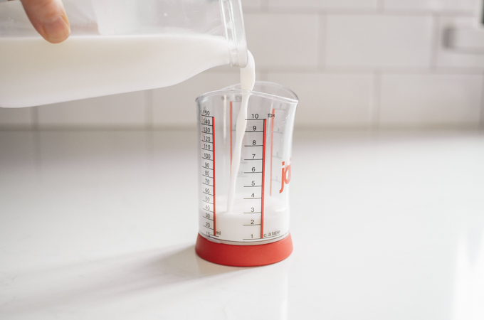 Pouring milk into a small measuring cup.