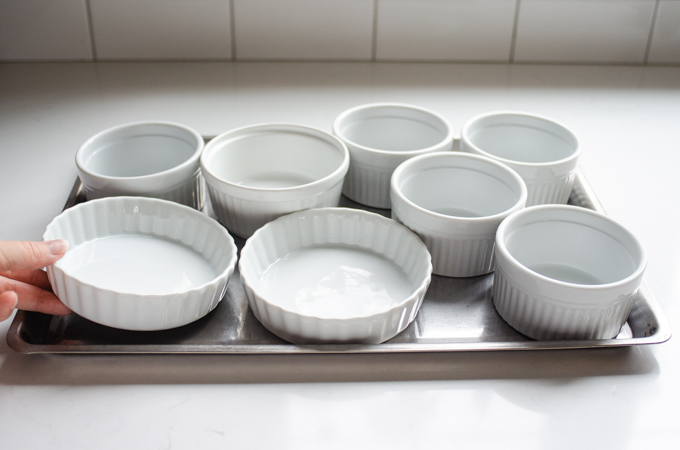 Lining a shallow rimmed baking sheet with ramekins. 