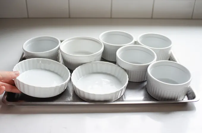 Lining a shallow rimmed baking sheet with ramekins. 