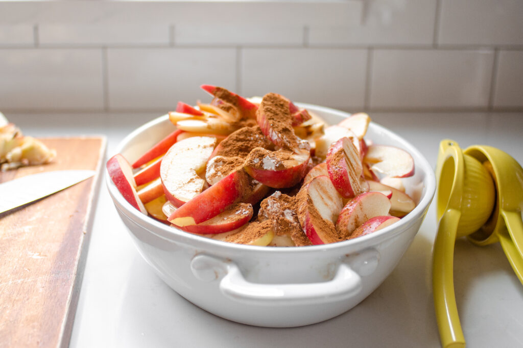 The sliced apples along with the cinnamon, maple syrup, cornstarch, lemon juice, and salt in an oval baking dish.