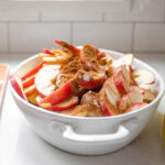 The sliced apples along with the cinnamon, maple syrup, cornstarch, lemon juice, and salt in an oval baking dish.