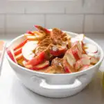 The sliced apples along with the cinnamon, maple syrup, cornstarch, lemon juice, and salt in an oval baking dish.
