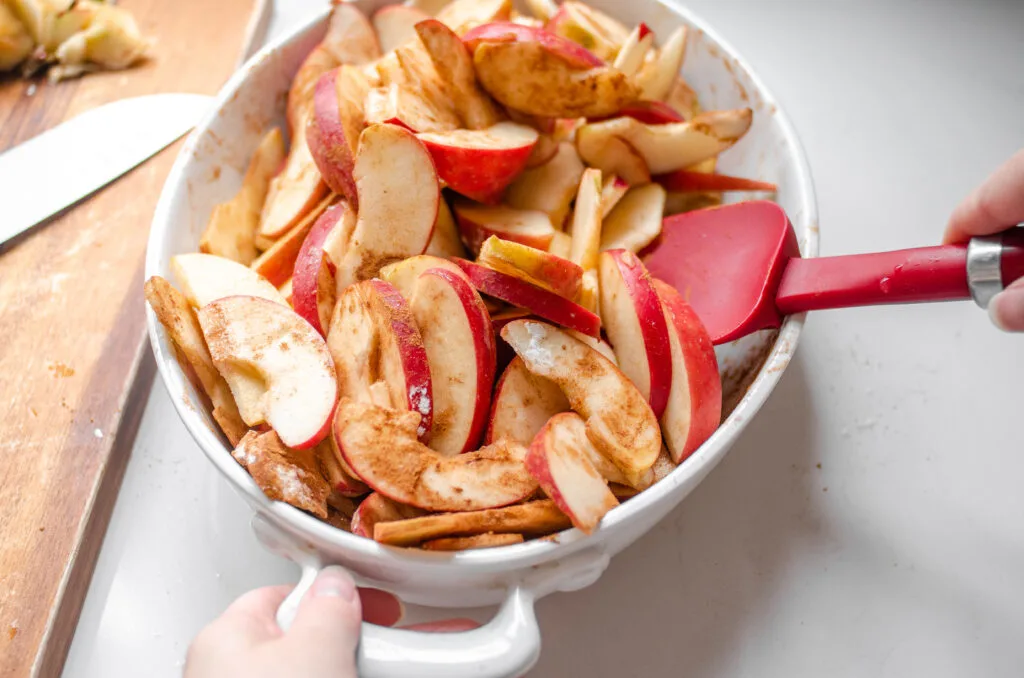 Tossing the cinnamon apple slices together in the baking dish to evenly coat the apples.