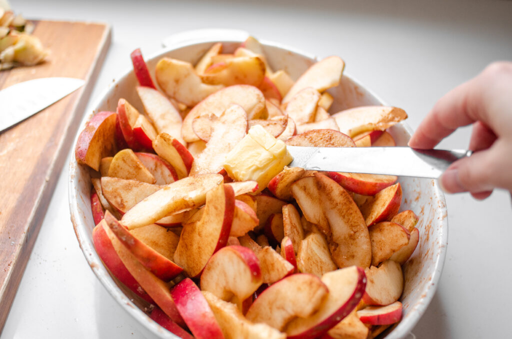 Putting butter on top of the cinnamon apples in the baking dish.