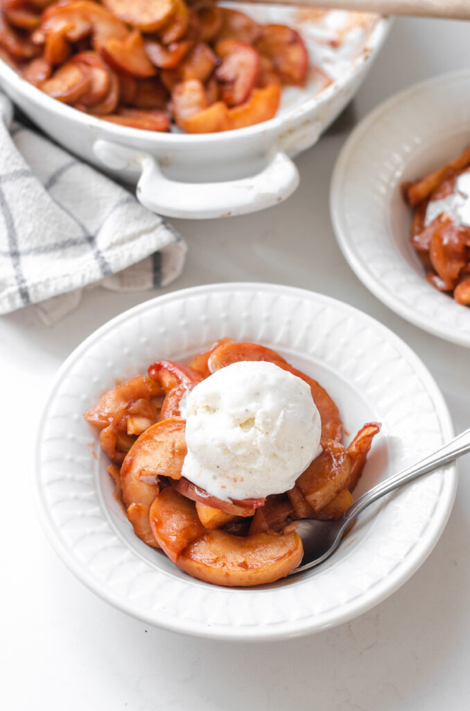 A bowl of baked cinnamon apples with a scoop of vanilla ice cream on top.