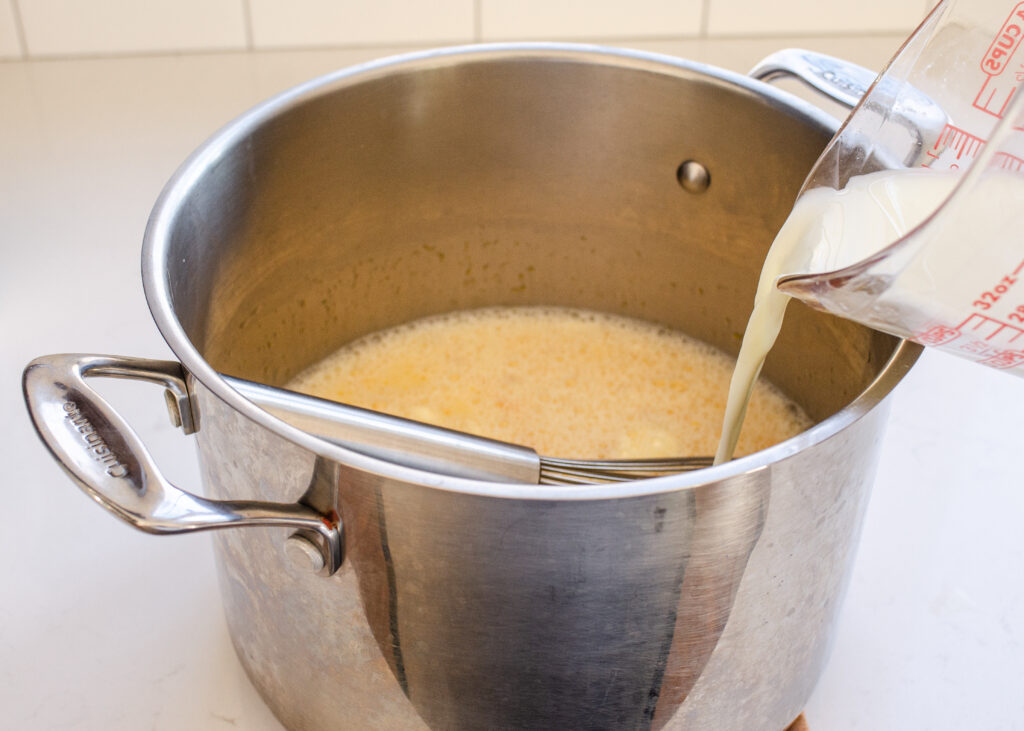 Adding half of the milk to the egg and maple syrup mixture in the pot.