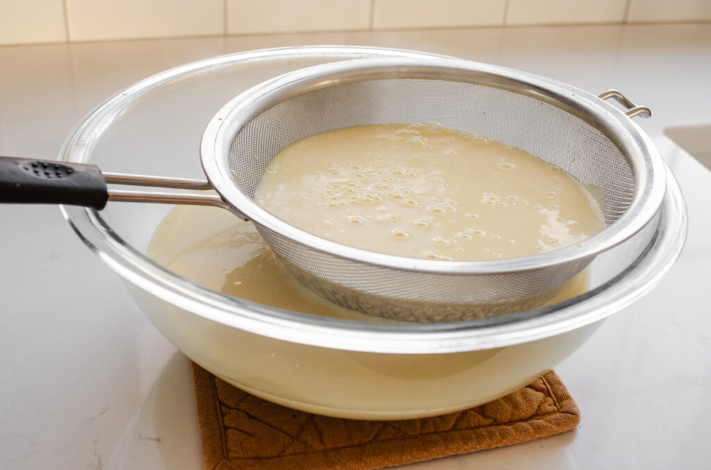 Straining the cooked eggnog custard to remove any lumps.