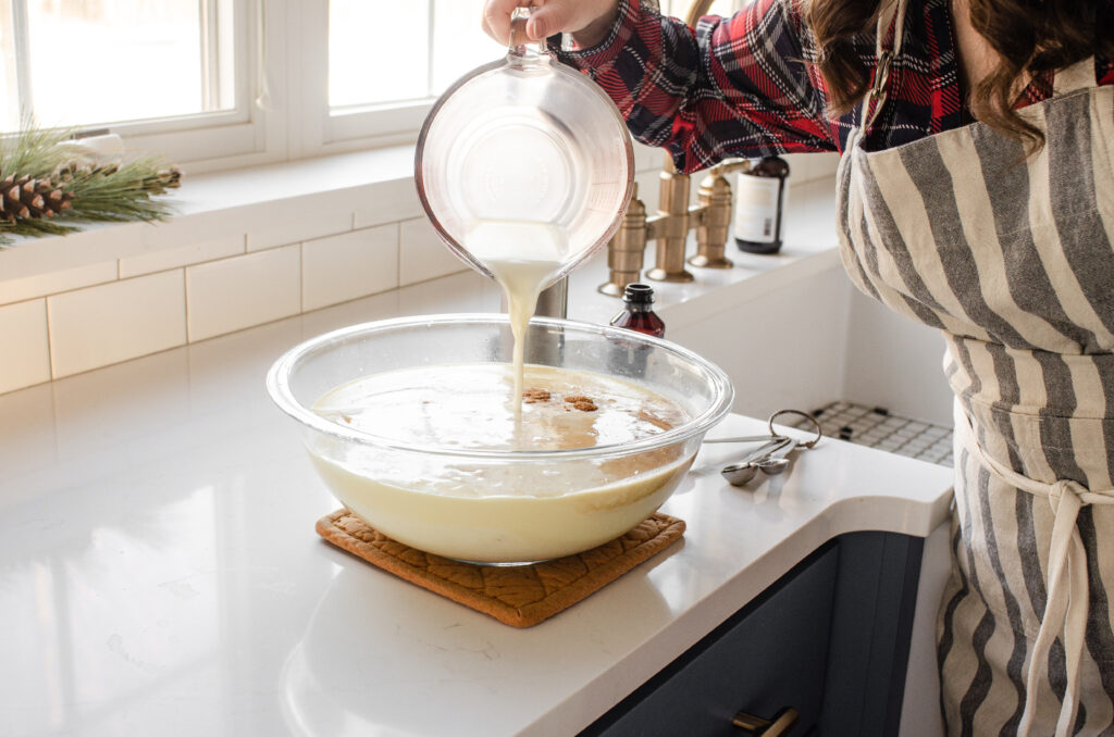 Pouring the remaining milk into the non-alcoholic eggnog custard mixture.