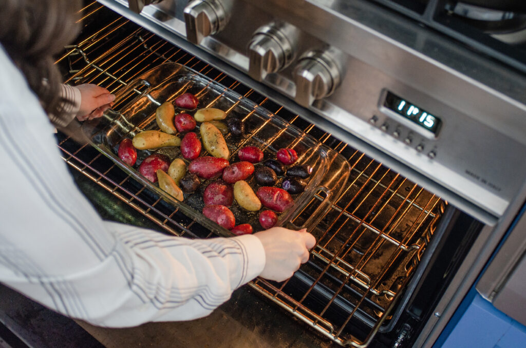 Placing the pan of mini potatoes in the oven to roast.