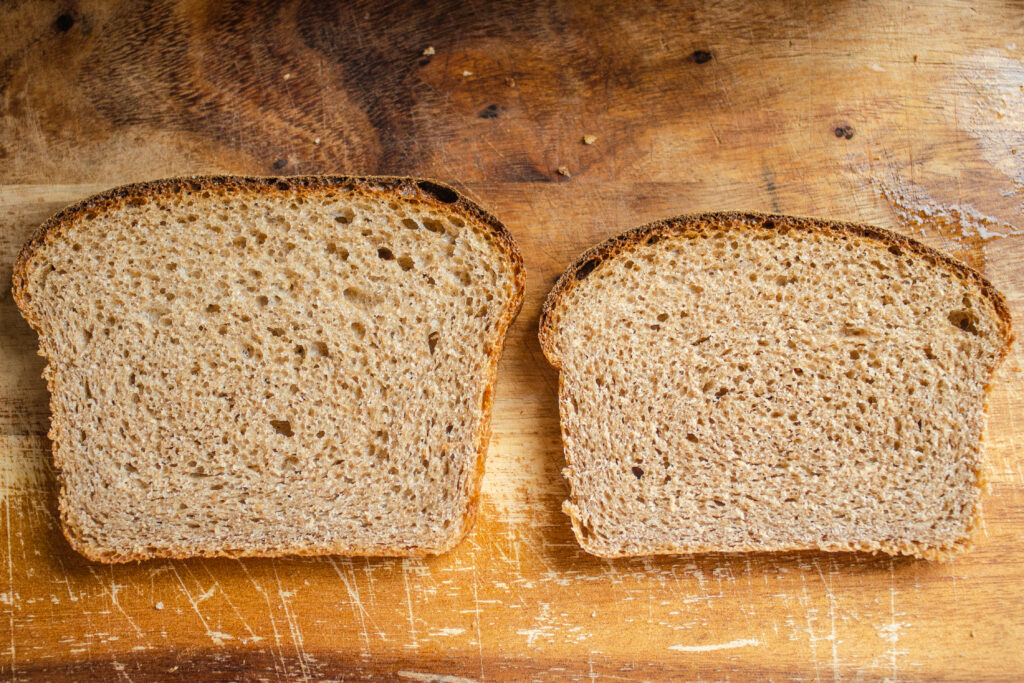 A side by side comparison of whole wheat sourdough breads. On the left is a slice of bread from a loaf risen with a white flour starter, and on the right is a slice risen from a whole wheat sourdough starter.