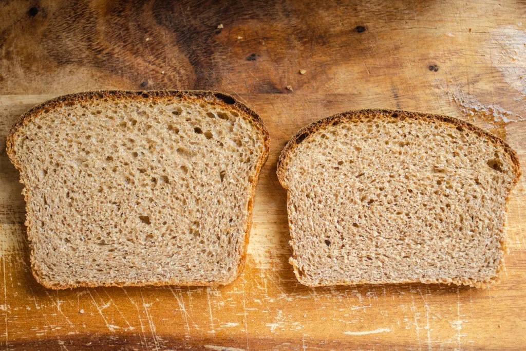 A side by side comparison of whole wheat sourdough breads. On the left is a slice of bread from a loaf risen with a white flour starter, and on the right is a slice risen from a whole wheat sourdough starter.