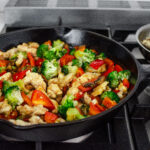 A large cast iron skillet filled with healthy chicken stir fry with loads of veggies.