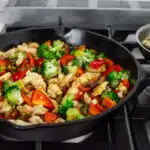 A large cast iron skillet filled with healthy chicken stir fry with loads of veggies.