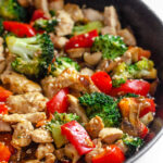 A large cast iron skillet filled with healthy chicken stir fry with loads of veggies.