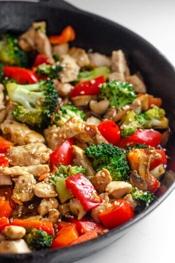 A large cast iron skillet filled with healthy chicken stir fry with loads of veggies.