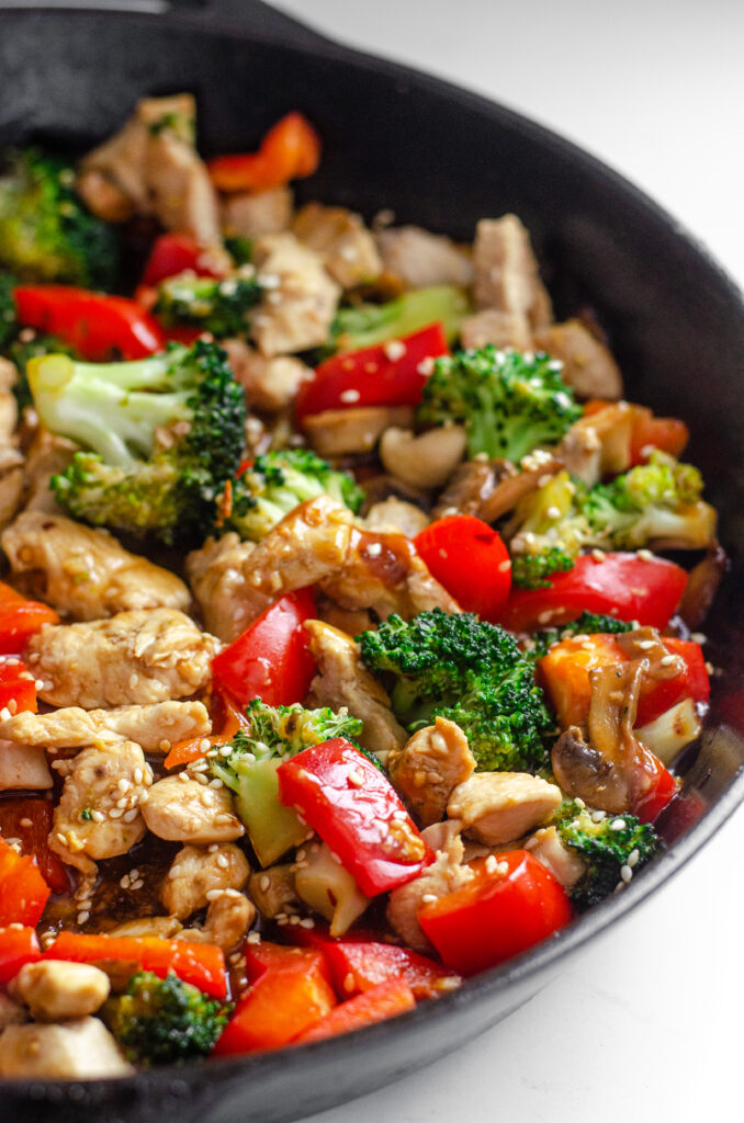 A large cast iron skillet filled with healthy chicken stir fry with loads of veggies.