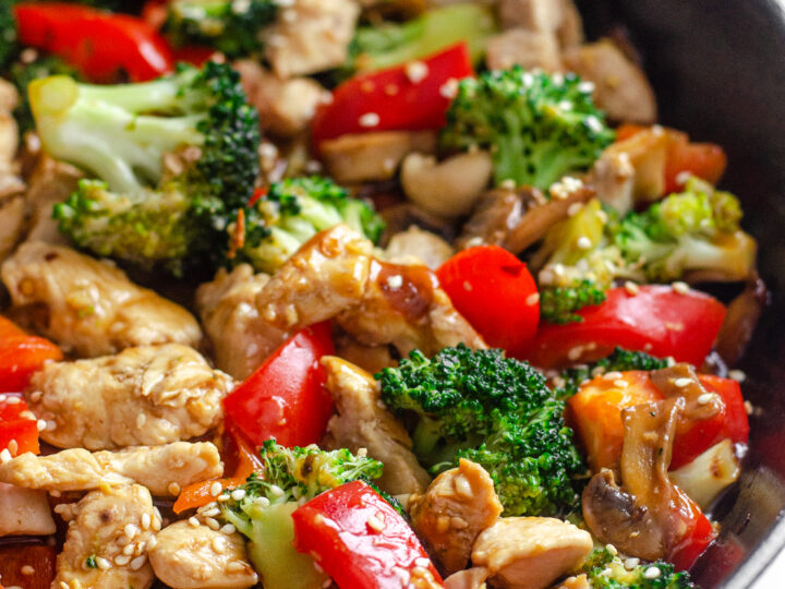 A large cast iron skillet filled with healthy chicken stir fry with loads of veggies.