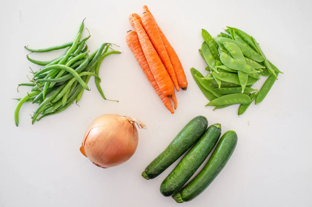 Different kinds of vegetables that you can use to make a stir-fry laid out on a white counter. 