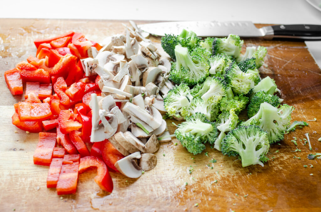 Red bell pepper, mushrooms, and broccoli sliced and prepared for a stir-fry. 