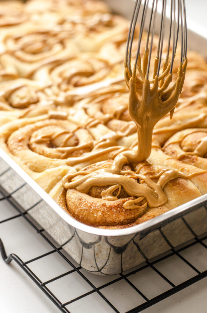 Drizzling the icing over the cooled cinnamon rolls. 