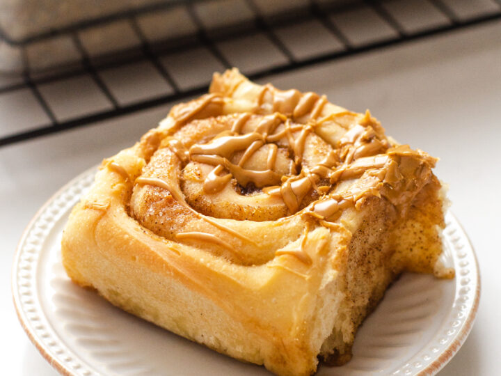 A dairy free cinnamon roll on a plate with the pan of cinnamon rolls in the background.