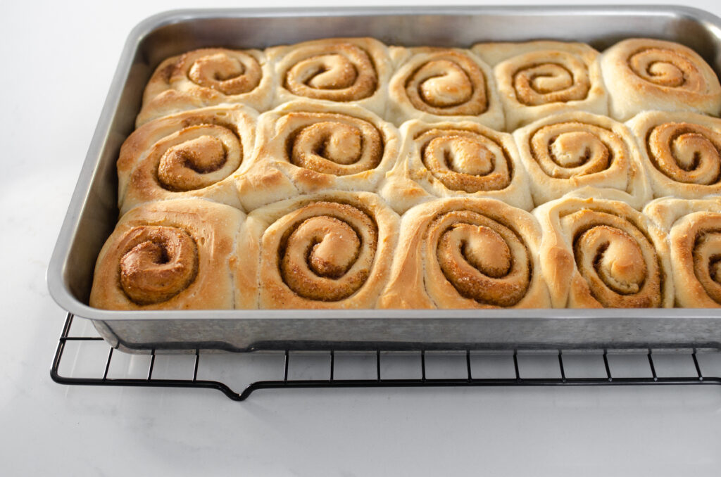 The baked cinnamon rolls without milk in a pan on a wire cooling rack.