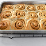 The baked cinnamon rolls without milk in a pan on a wire cooling rack.