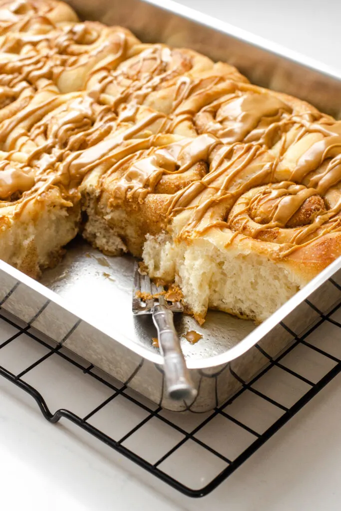 A pan of cinnamon rolls without milk with a couple of rolls taken out and a fork in the pan.