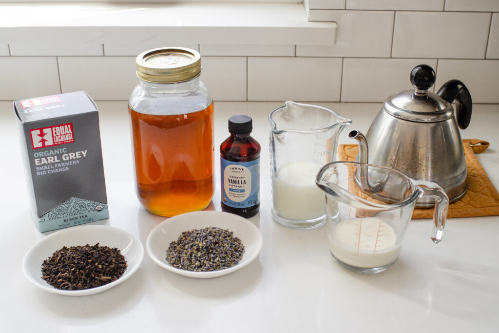 All of the ingredients needed to make an earl grey tea latte laid out on a white countertop. 