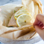 A salmon filet in a piece of parchment paper with snow peas underneath and slices of lemon on top.