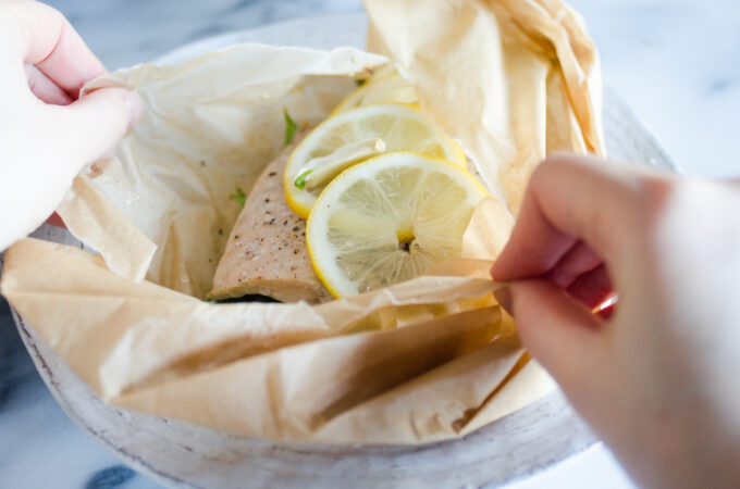A salmon filet in a piece of parchment paper with snow peas underneath and slices of lemon on top.