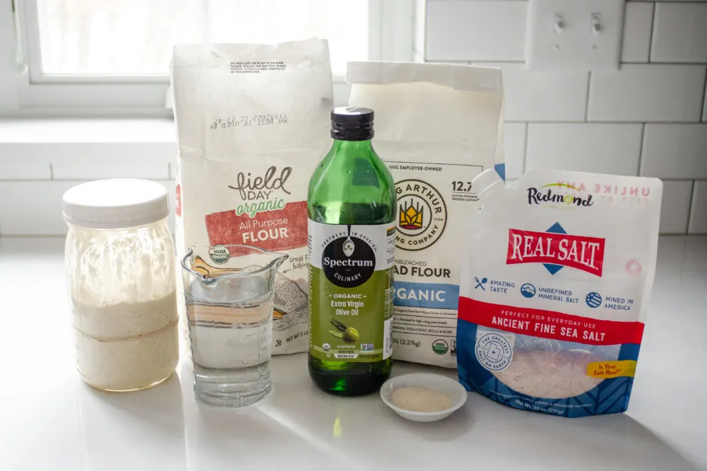 All of the ingredients needed to make a sourdough pizza crust without yeast on a white countertop.