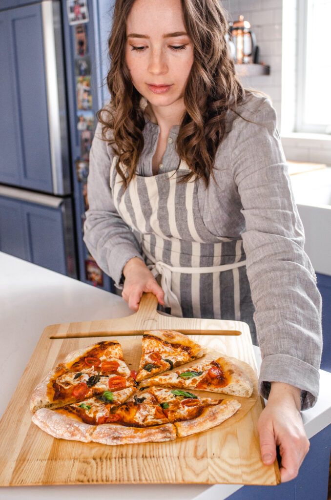 Removing the cooked sourdough pizza from the oven onto a cutting board.