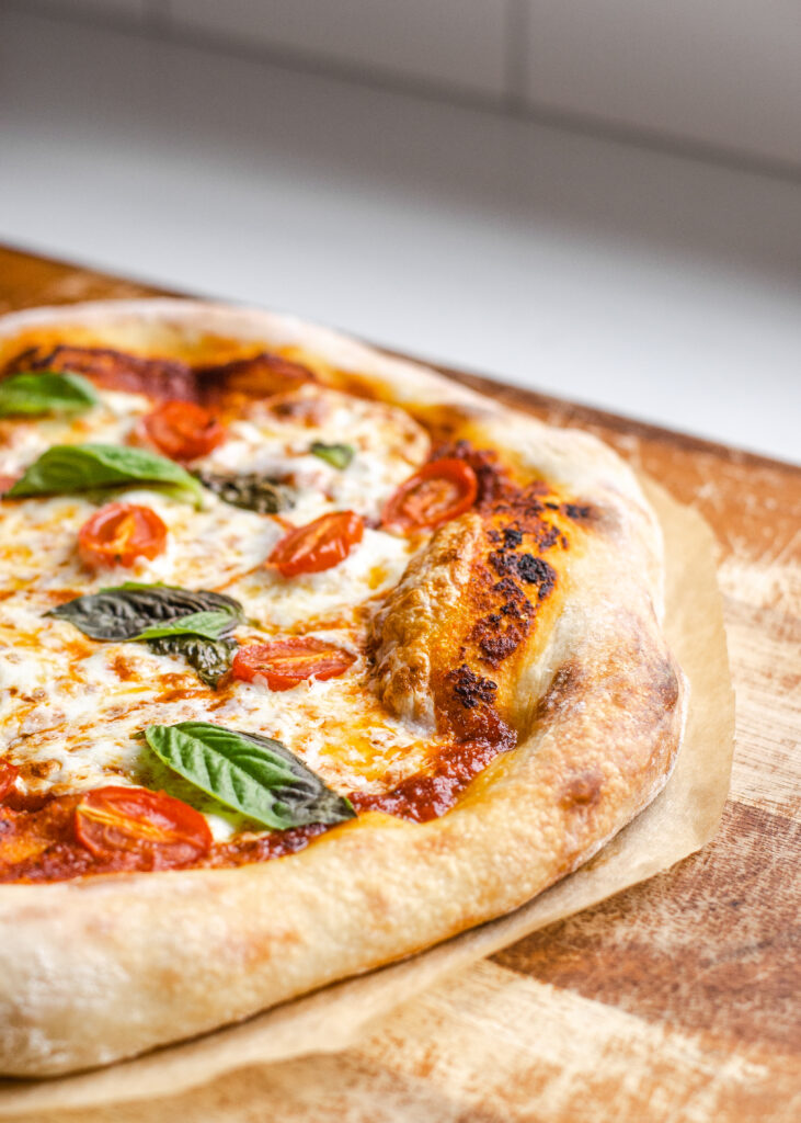 A sourdough pizza crust topped with fresh mozzarella, fresh basil, tomatoes, and a red sauce. 