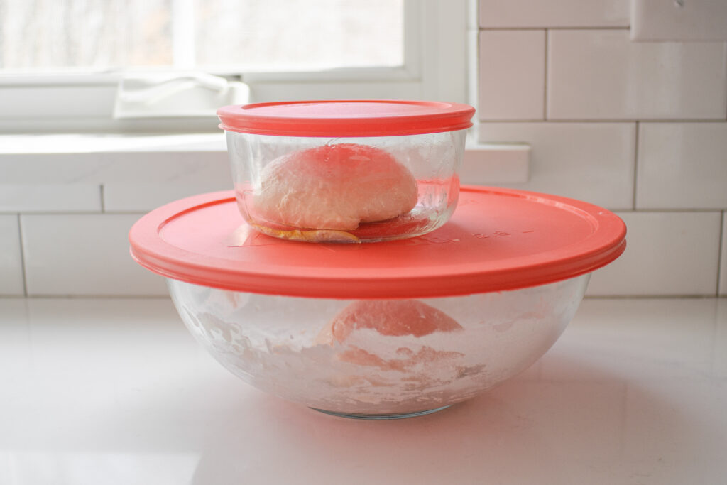 Placing the sourdough pizza dough in greased lidded containers. 