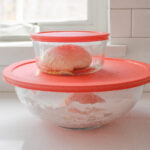 Placing the sourdough pizza dough in greased lidded containers.