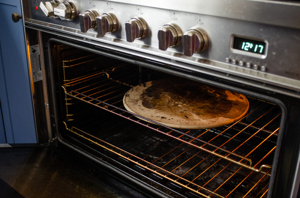 Placing a pizza stone in an oven to preheat for baking the sourdough pizza crust. 