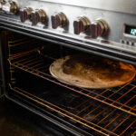 Placing a pizza stone in an oven to preheat for baking the sourdough pizza crust.