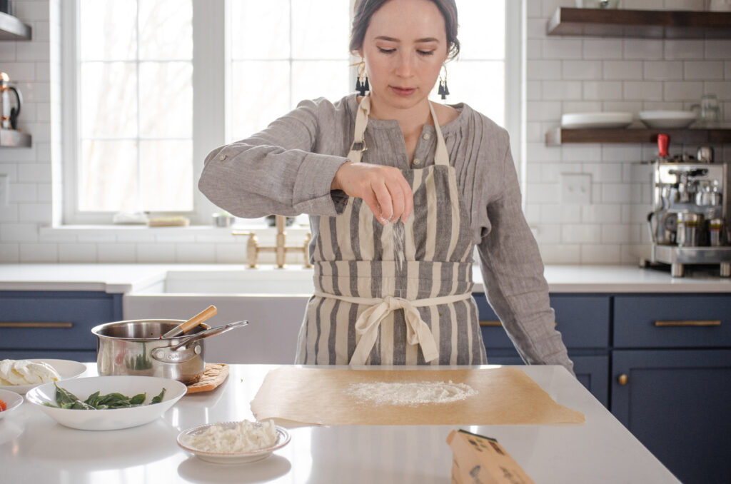 Dusting a piece of parchment paper with flour in preparation for shaping the sourdough pizza crust. 