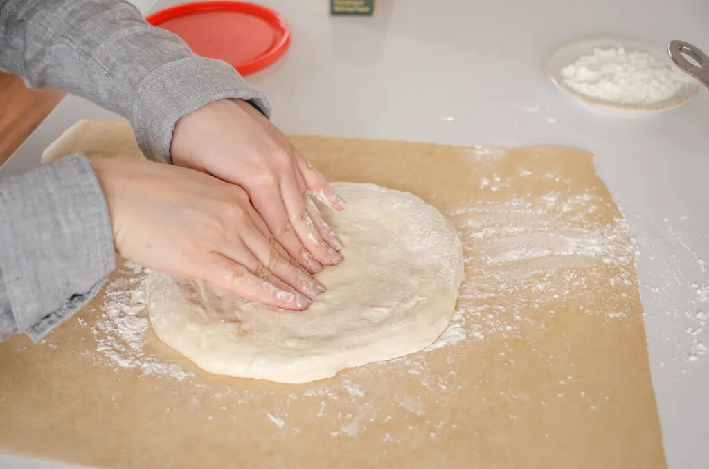 Shaping the sourdough pizza dough on a sheet of floured parchment paper.