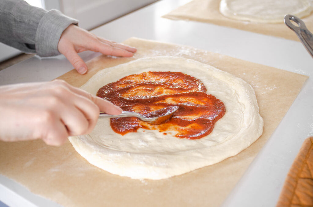 Spreading the pizza sauce on the prepared dough.