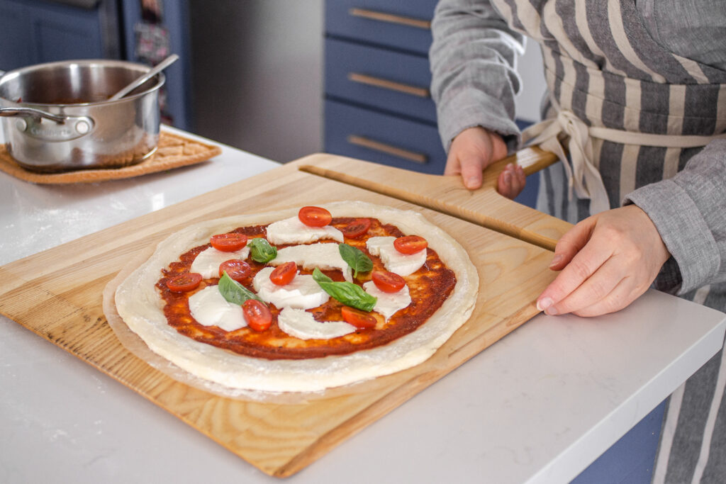 Transferring the topped sourdough pizza crust onto a pizza peel to transfer to the oven.