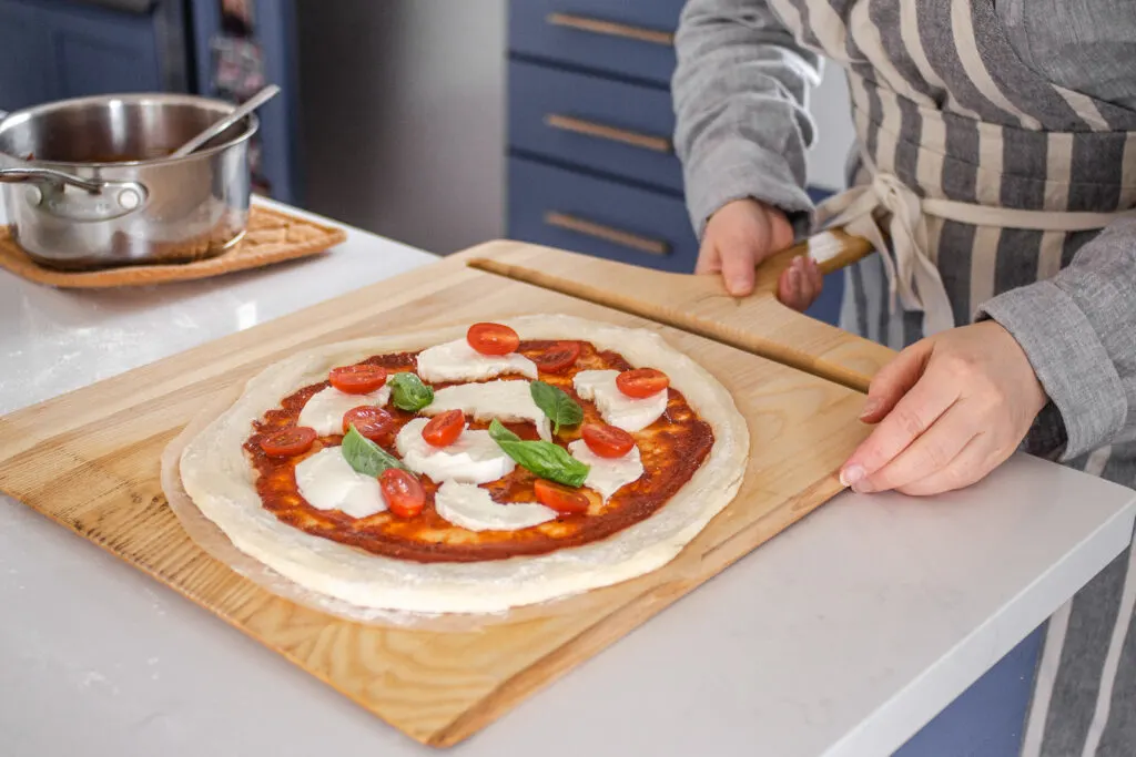 Transferring the topped sourdough pizza crust onto a pizza peel to transfer to the oven.