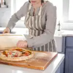 Removing the cooked sourdough pizza from the oven onto a cutting board.