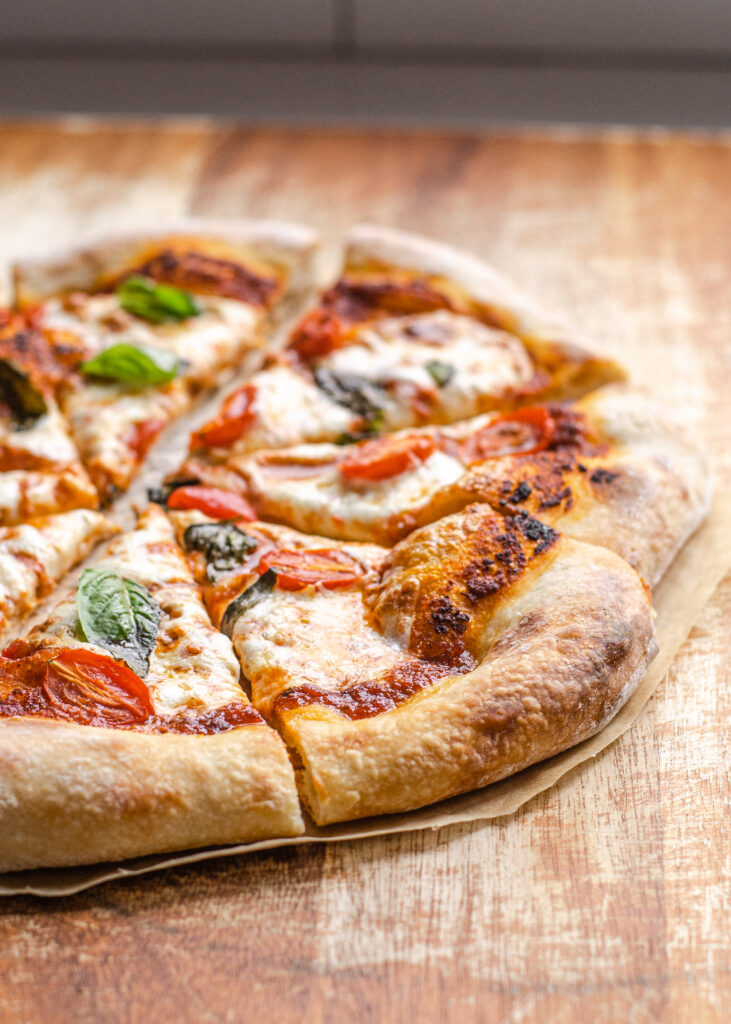 Pizza with a sourdough crust on a wooden cutting board cut into pieces. 