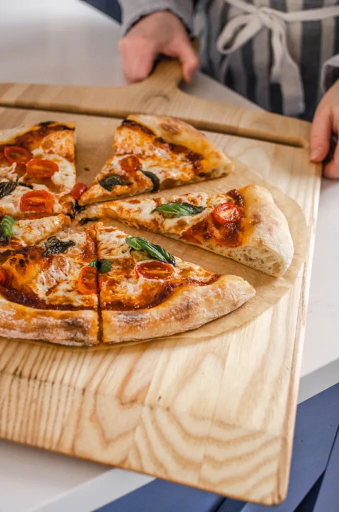 Removing the cooked sourdough pizza from the oven onto a cutting board.