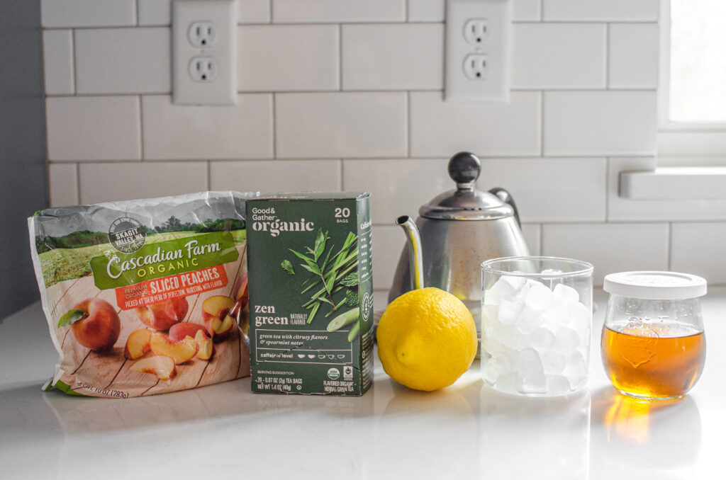 All of the ingredients needed to make a peach green tea lemonade (Starbucks Copycat) laid out on a white counter.