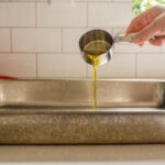 Pouring extra virgin olive oil into a pan to grease it in preparation for putting the focaccia dough in it.