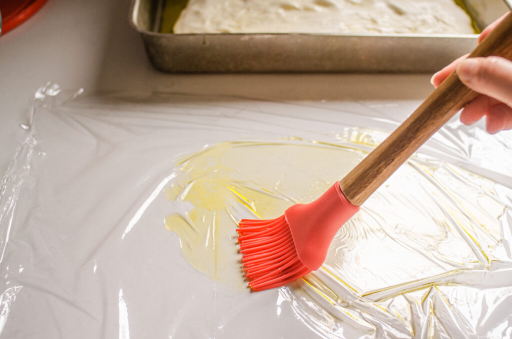 Greasing a piece of plastic wrap with olive oil to put on top of the focaccia dough.